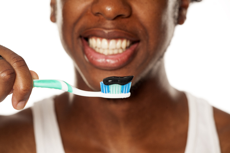 portrait of a happy young dark-skinned man posing with toothbrush and black tooth paste on a white backgroundの写真素材
