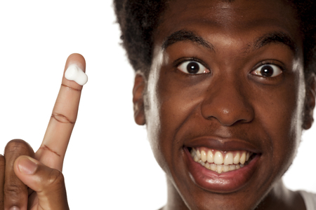 Young african-american guy showing cosmetics cream on his finger on white backgroundの写真素材