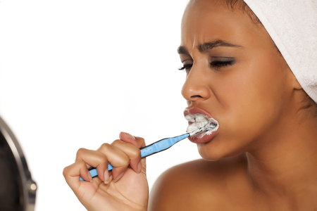 portrait of a young dark-skinned woman brushing her teeth on a white backgroundの写真素材