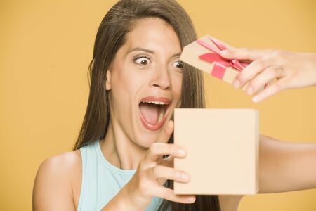 Young happy woman opening a present box on yellow backgroundの写真素材