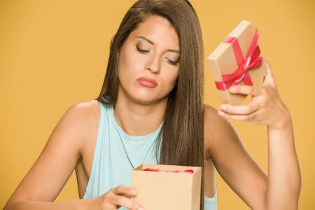 Young disappointed woman opening a present box on yellow backgroundの写真素材