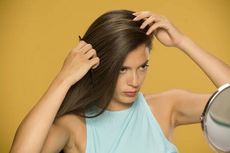 Young beautiful woman combing her hair on yellow backgroundの写真素材