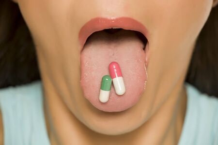 Closeup of woman holding capsules on her tongueの写真素材