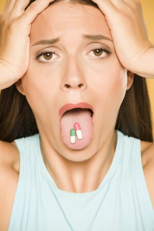 Unhappy young woman holding capsules on her tongueの写真素材