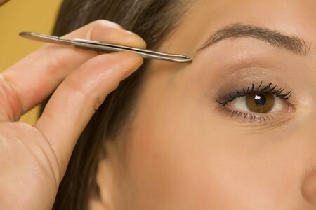 closeuo of woman plucking her eyebrows with tweezersの写真素材
