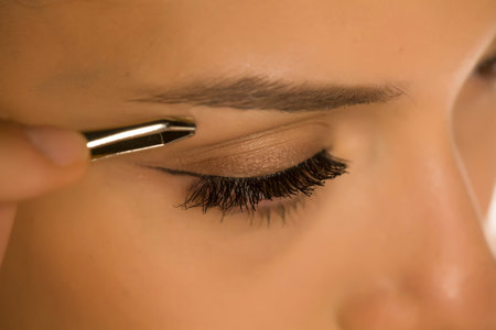 closeup of woman plucking her eyebrows with tweezers