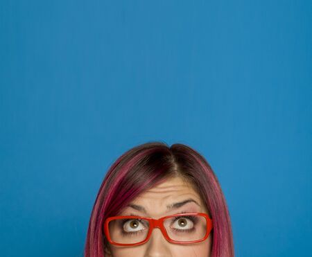 Half portrait of a young worried woman with pink hair and glasses on blue backgroundの写真素材