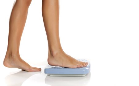Young woman standing on a scale on white backgroundの写真素材