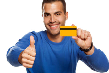 portrait of happy young man, holding empty credit card on white background and showing thumbs upの写真素材