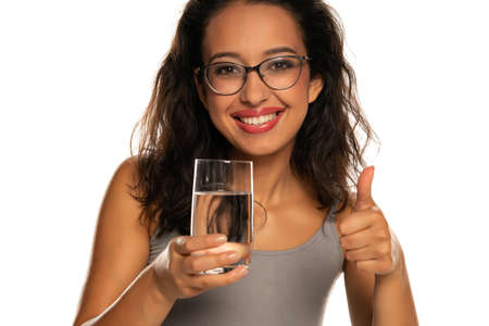 Young dark skinned woman with glass of water on white backgroundの写真素材