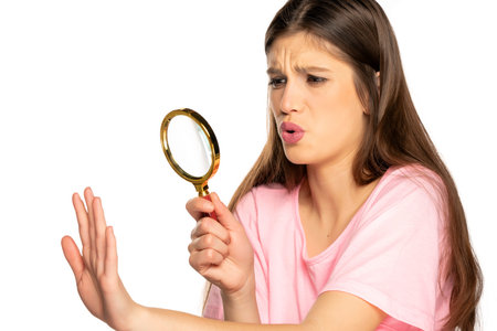 Young worried woman looking her nails with magnifying glass on white background
