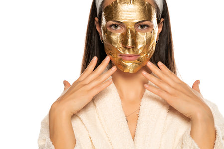 young woman posing with golden mask on her face on white backgroundの写真素材