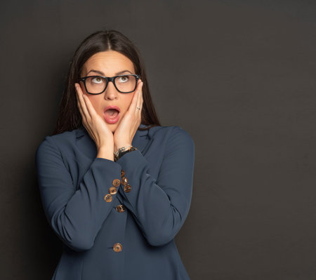 Attractive shocked business woman in blue suit  posing on black wall