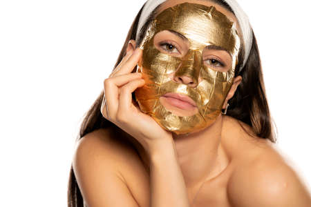 young woman posing with golden mask on her face on white backgroundの写真素材