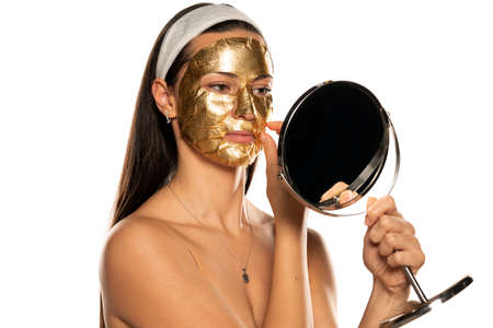 young woman putting on a golden mask on her face on white backgroundの写真素材