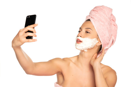 Young funny woman with shaving foam on her face, take a selfies on white background