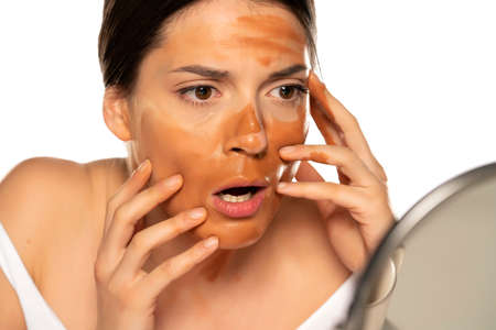 Young shocked woman with wrong makeup base on her face on white backgroundの写真素材