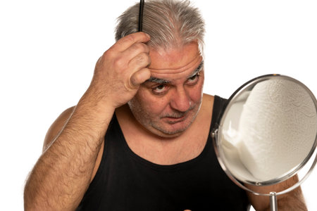 middle aged man combing his short gray hair on white background