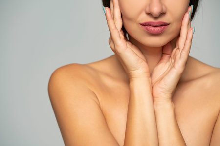 close up of a young beautiful smiling woman touches her face on a gray background