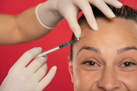 Portrait of a young smiling woman on a face filler injection procedure on red backgroundの写真素材