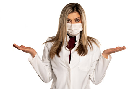 Young nervous female doctor with  face medical mask and questionable gesture on a white backgroundの写真素材