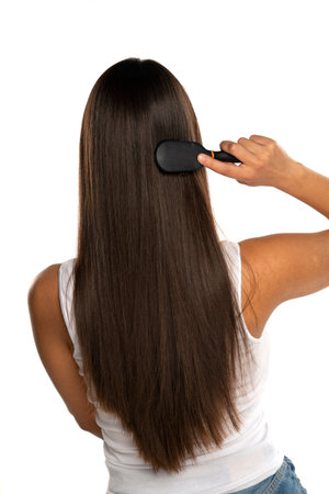 rear view of a young woman brushing her straight long hair on a white background