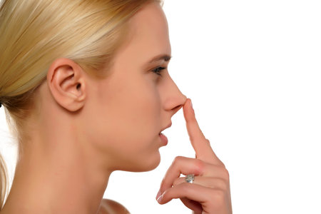 Young blond woman touches her nose with her finger on a white background