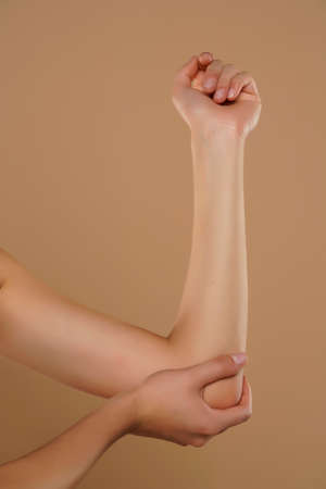 Woman hold her aching elbow on a beige backgroundの写真素材
