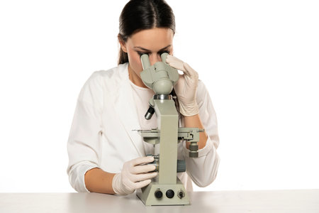 a young female scientist looks through a microscope in a studio on a white background