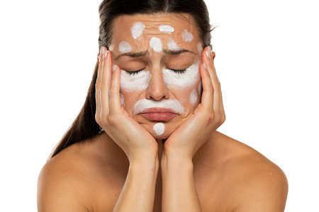Unhappy sad woman posing with face cream on a white backgroundの写真素材