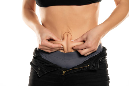 Closeup of a young fit woman pinching her belly on a white background.