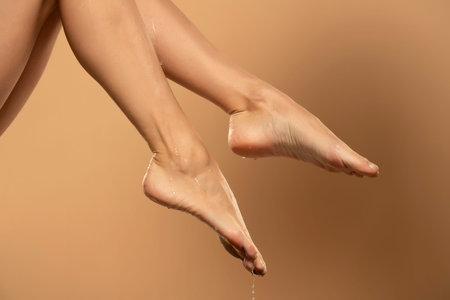 Close up of a female wet legs and feet with water gliding over them  on a beige background