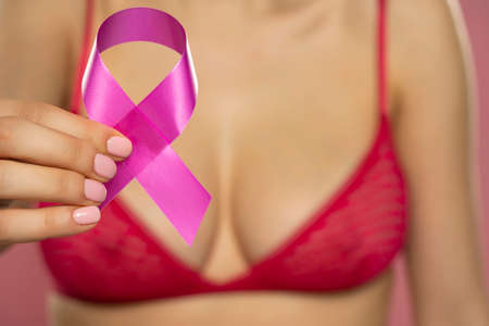 Close up young woman in shirt holding cancer awareness ribbon on pink backgroundの写真素材