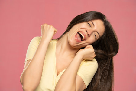 Studio portrait of excited young woman cheering on a pink backgroundの写真素材