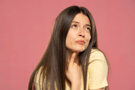 Portrait of young attractive beautiful thoughtful woman thinking look copyspace isolated on pink color backgroundの写真素材
