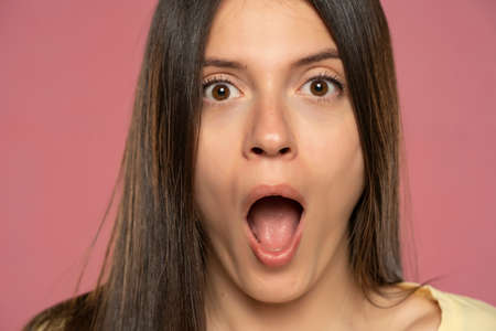 Close-up portrait of young amazed woman  on a pink backgroundの写真素材