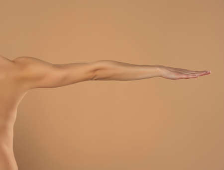 Young woman's stretched arm and palm. Isolated on beige background.の写真素材