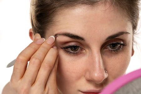 Young woman plucking eyebrows with tweezers close up.の写真素材