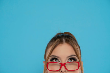 half portrait of a young woman with glasses looking up on a bluse background.の写真素材