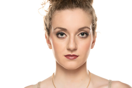 Young blond woman with curly tied hair and makeup posing on white background.の写真素材