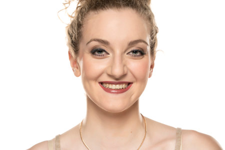 Young blond smiling woman with curly tied hair and makeup posing on white backgroundの写真素材