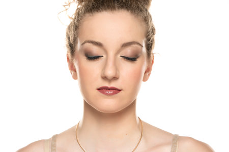 Young blond woman with curly tied hair and makeup posing on white background. eyes closedの写真素材