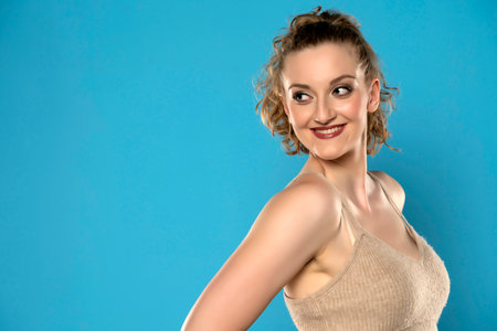 Attractive blonde woman with tied curly hair smiling on blue backgroundの写真素材