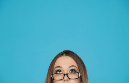 half portrait of a young woman with glasses looking up on a blue background.