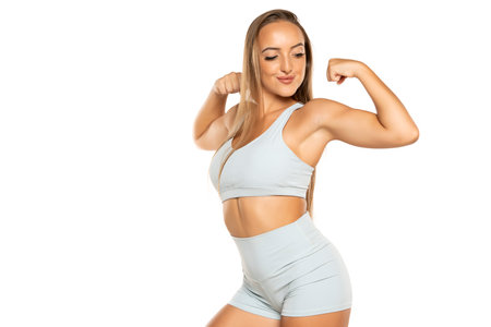 young sports woman with long hair in a shorts and top showing biceps on a white studio backgroundの写真素材