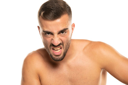 portrait of young angry shirtless man with beard, screaming on a white studio backgroundの写真素材
