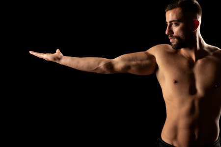 Torso of a young athletic guy with outstretched hand. concept: the male body after exercise and diet. men's health: shaved breasts on a dark studio backgroundの写真素材