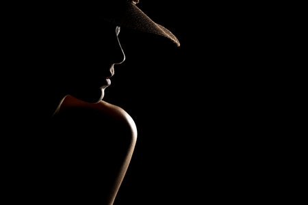 Sensual portrait silhouette of beautiful woman with a hat in backlight on a black studio backgroundの写真素材