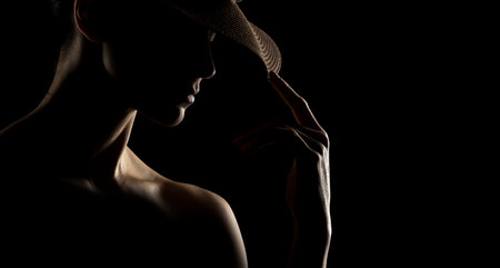 Sensual portrait silhouette of beautiful woman with a hat in backlight on a black studio backgroundの写真素材