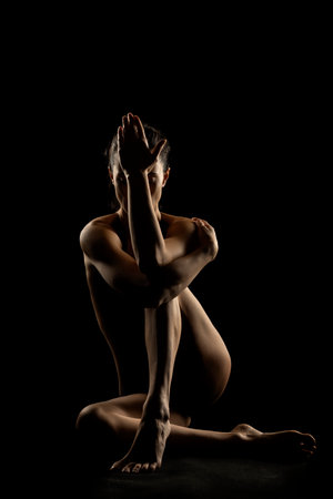 Silhouette of unrecognizable nude woman posing in the shadows on a black studio backgroundの写真素材